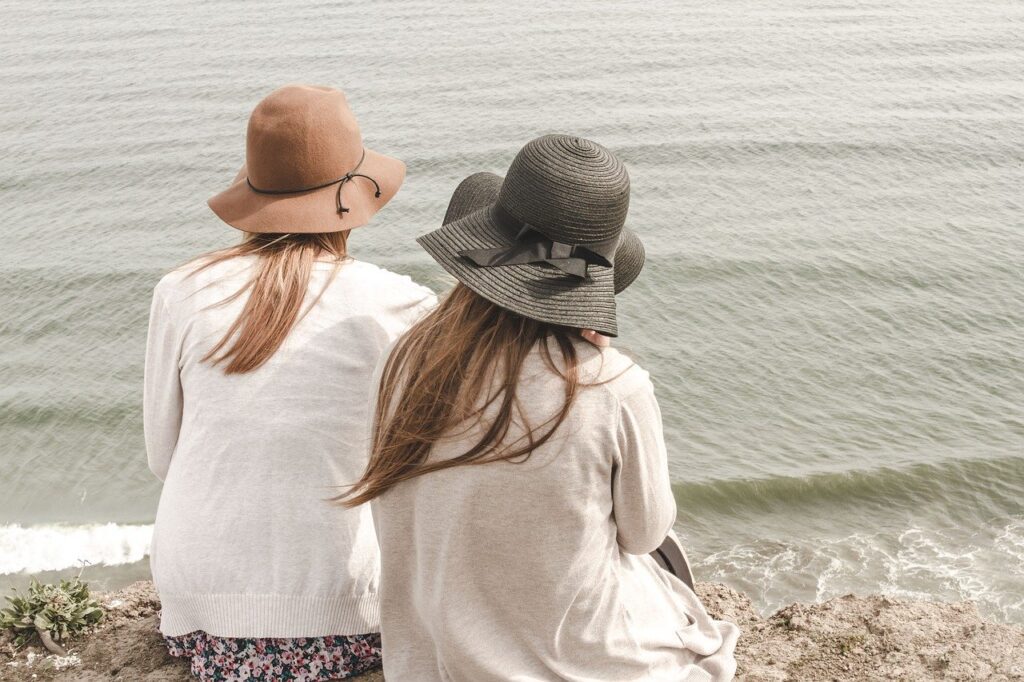 Two girls with hats are sitting on the beach